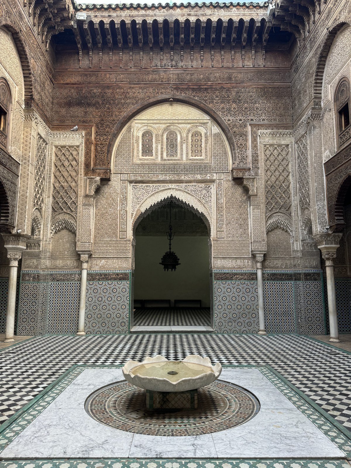 Courtyard fountain, zellige floor and carved doorway at Al Attarine Madrasa in Fes